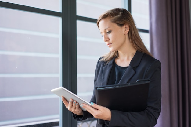 Closeup portrait of serious young beautiful brown-haired business woman using tablet 