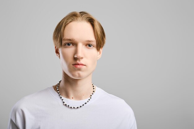 Closeup portrait of serious young man in white tshirt over gray studio background