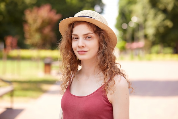 Ritratto del primo piano di bella donna sorridente che posa in aria fresca, con piacevole espressione facciale, in piedi intorno a numerosi alberi