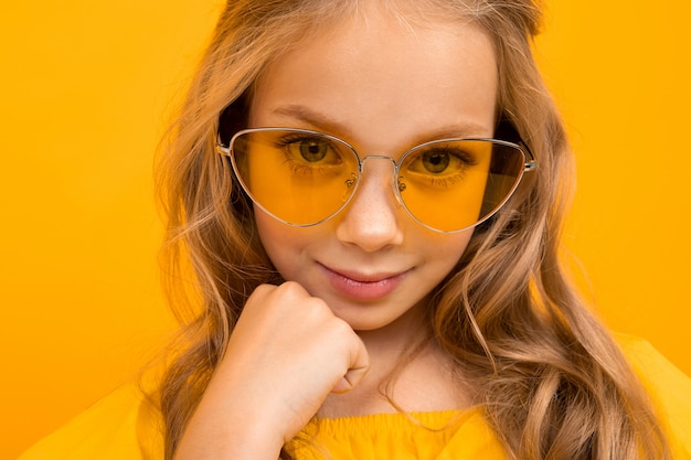 Closeup portrait of a smiling blonde in glamorous glasses on a yellow background