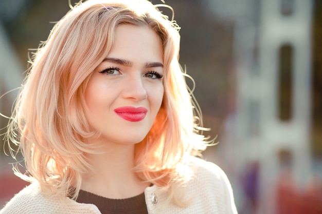 Closeup portrait of smiling blonde model with bright makeup and perfect skin posing in sunny day