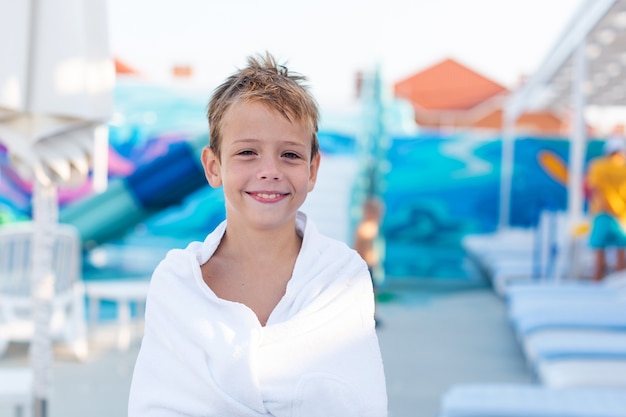 Closeup portrait of a smiling boy wrapped in a towel after swimming in the outdoor pool