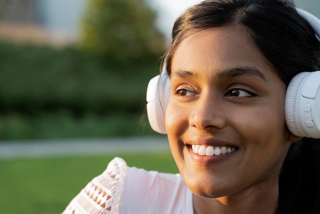 Крупным планом портрет улыбающейся индийской женщины в беспроводных наушниках, слушающей музыку в парке