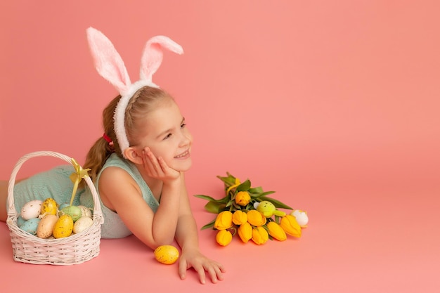 Closeup portrait of a smiling little girl on a pink background with an easter decor Copy space