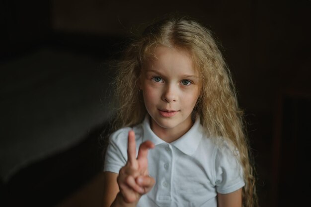 Photo closeup portrait of a smiling little girl showing bunny ears with her fingers