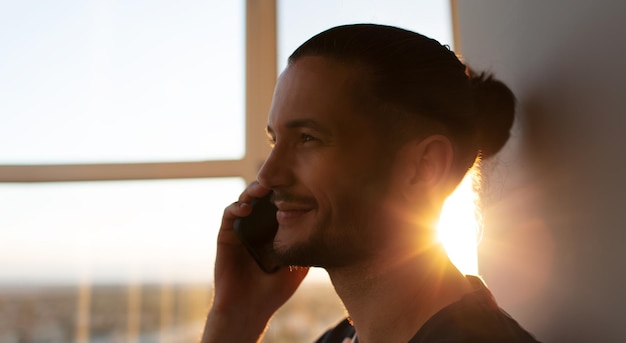 Ritratto del primo piano dell'uomo sorridente che parla sullo smartphone sullo sfondo del tramonto