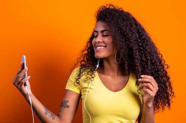 Closeup portrait of smiling young attractive African brazilian woman holding smartphone, taking selfie photo