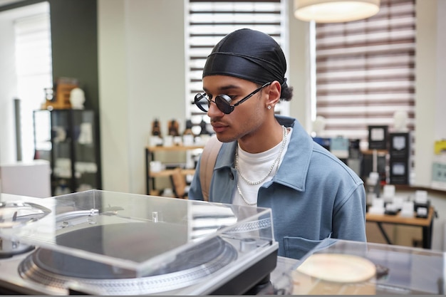 Closeup portrait of stylish young black man looking at vinyl record player in music store copy space