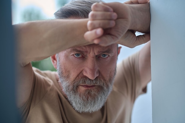 Closeup portrait of a sulky lonely gray-haired mature male leaned against the wall staring ahead