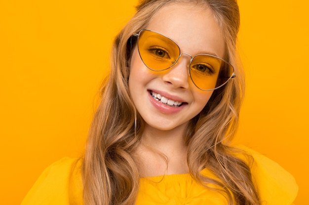 黄色の背景にレトロなメガネで10代の少女のクローズアップの肖像画。