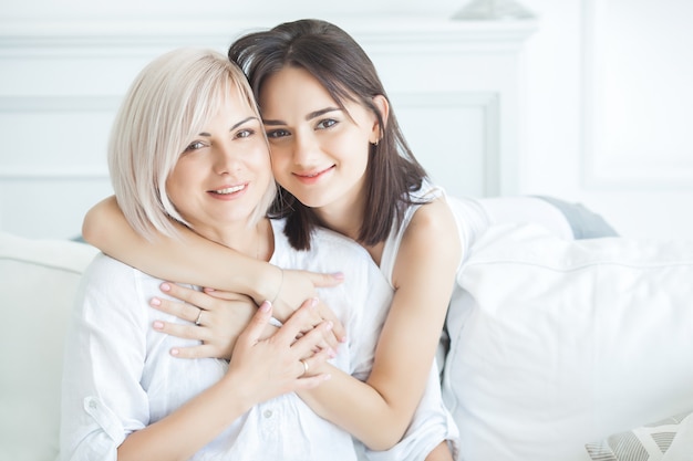 Closeup portrait of two beautiful women mom and daughter. Mid adult mother embracing her adult daughter indoors. Happy smiling females hugging.