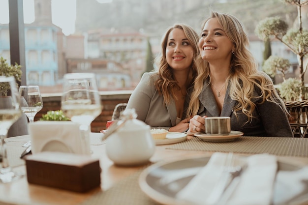 Closeup portrait of two female friends in strict suits laughing drinking coffee and wine on the