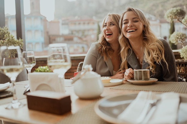 Closeup portrait of two female friends in strict suits laughing drinking coffee and wine on the