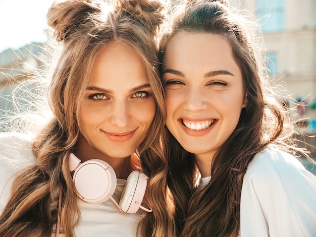 Closeup portrait of two young beautiful smiling hipster female in trendy summer white t-shirt clothes