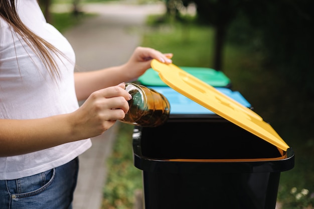 リサイクルビンに空のプラスチック製の水のボトルを投げるクローズアップの肖像画の女性の手