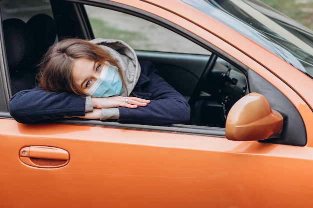 車の中で医療マスクの女性のポートレート、クローズアップ。コロナウイルスエピデミック。 SARS-CoV-2。 COVID-19を停止します。