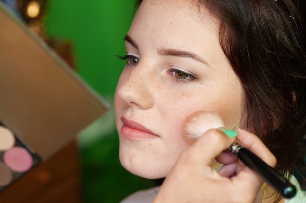 Closeup portrait of a woman, putting on makeup with brush