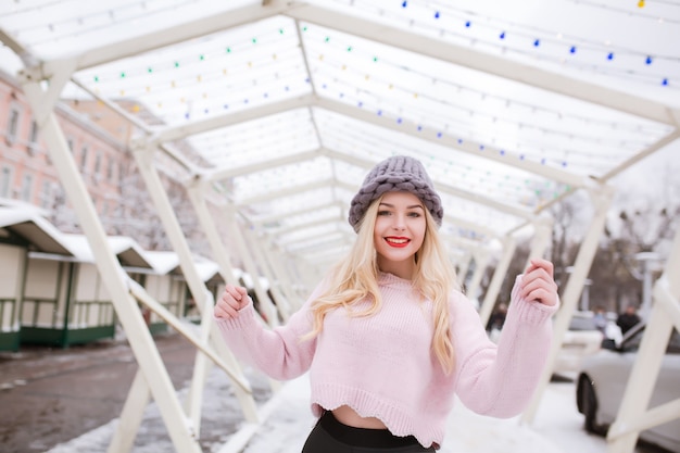 Closeup portrait of wonderful young model with bright makeup, wearing trendy knitted hat and sweater, posing at the city in winter