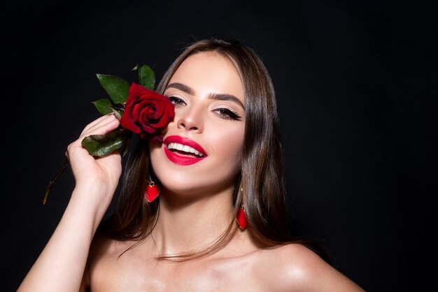 Closeup portrait of young beautiful sexy woman with red rose on a black background closeup fresh fac