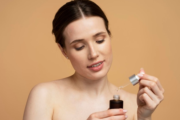 Closeup portrait of young beautiful smiling woman holding bottle with face serum