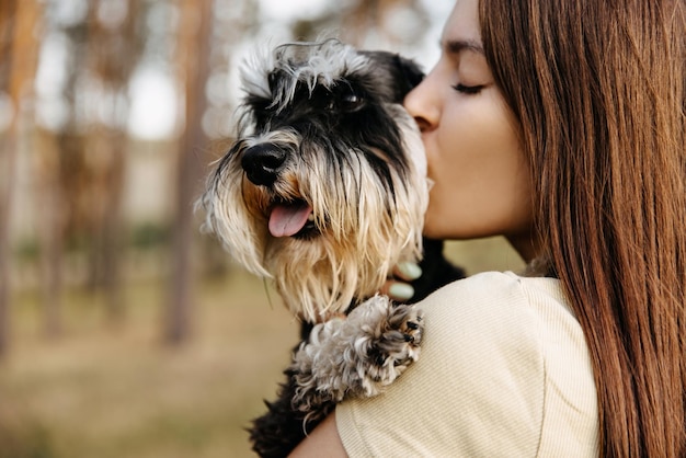 Closeup portrait of a young brunette woman hugging a miniature schnauzer breed dog kissing it