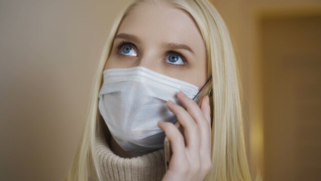 Closeup portrait of young girl in medical face mask is talking at phone