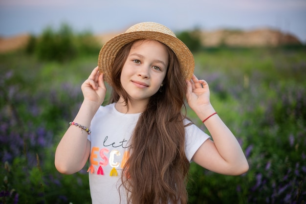 Closeup portrait of young girl with long hair and straw hat relaxing on blooming lupine field.