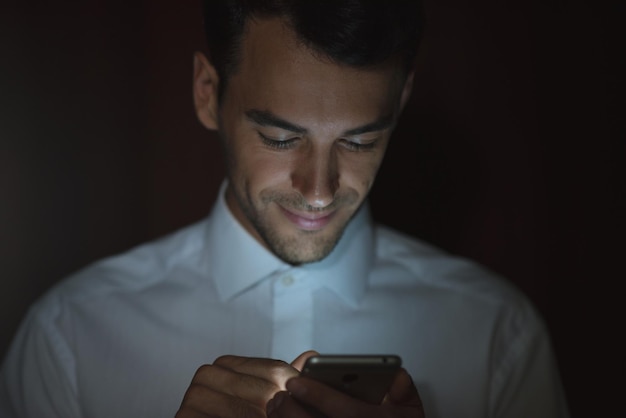 Крупным планом портрет молодого красивого мужчины с помощью смартфона в руке на темном фоне