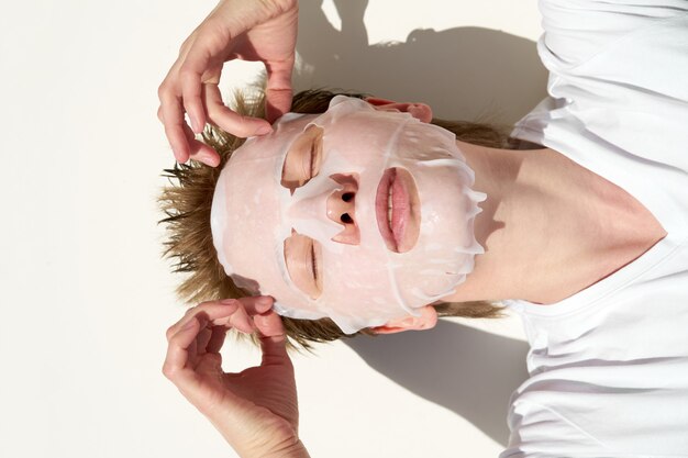 Closeup portrait young redhead woman with closed eyes applying tissue facial mask