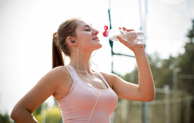 実行して水を飲むことで休憩を持つ若いスリムな女性のクローズ アップの肖像画