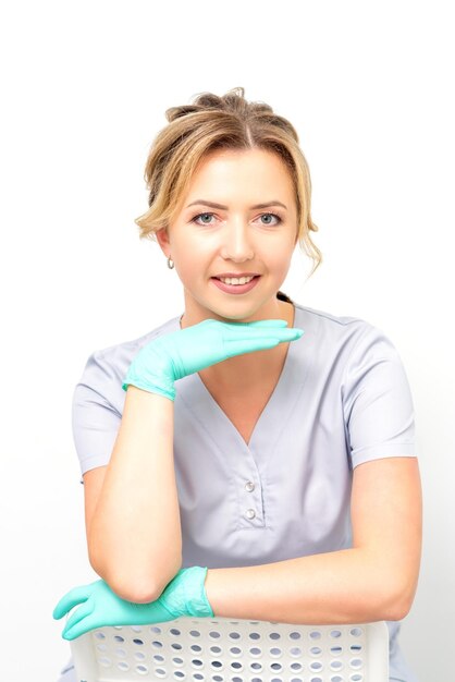 closeup portrait of young smiling female caucasian healthcare worker sitting and staring at the camera wearing gloves on white background