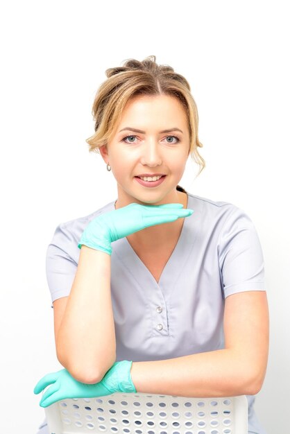 Closeup portrait of young smiling female caucasian healthcare worker sitting and staring at the camera wearing gloves on white background