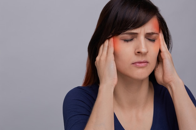 Closeup portrait of young woman on grey background suffering from strong headache