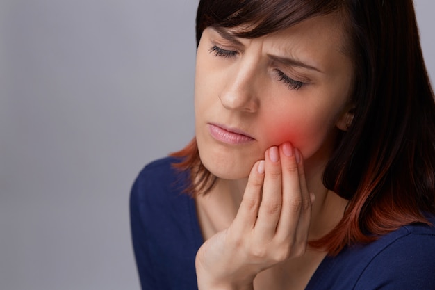 Foto ritratto del primo piano di giovane donna su fondo grigio che soffre di mal di denti.