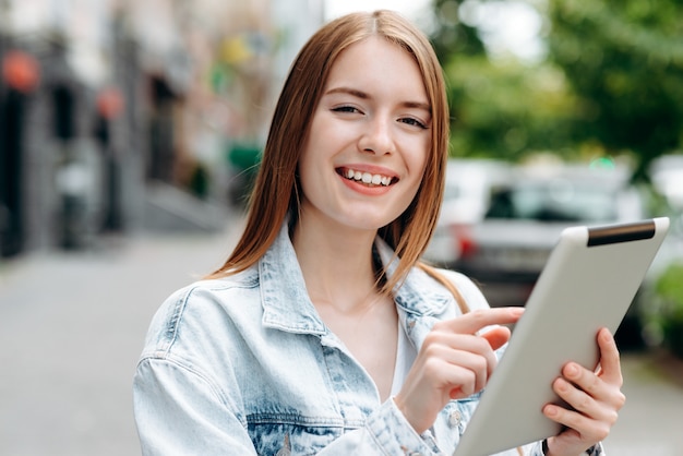 Photo closeup portrait of young woman holding an ipad and standing outdoor