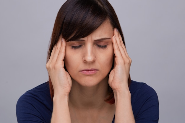  Closeup portrait of young woman suffering from strong headache, holding fingers to temples and closing eyes from pain. Severe migraine. 