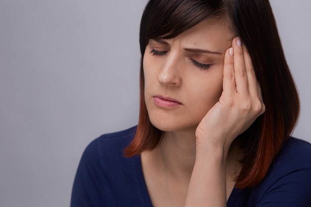 Closeup portrait of young woman suffering from toothache, holding fingers to jaw and closing eyes from pain. 