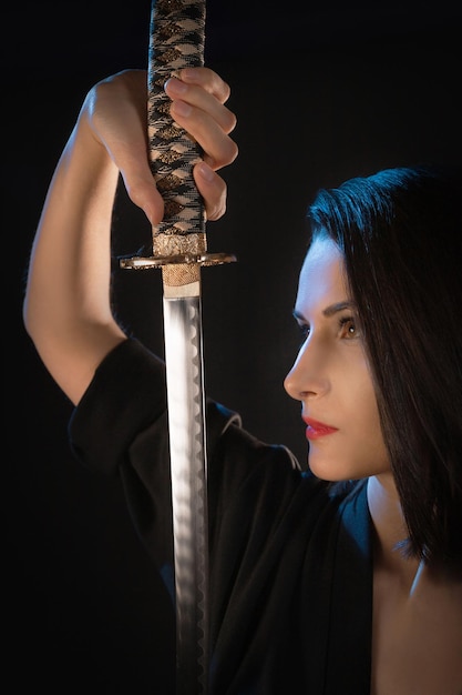 Closeup portrait of a young woman warrior with a katana looking at a sharp blade