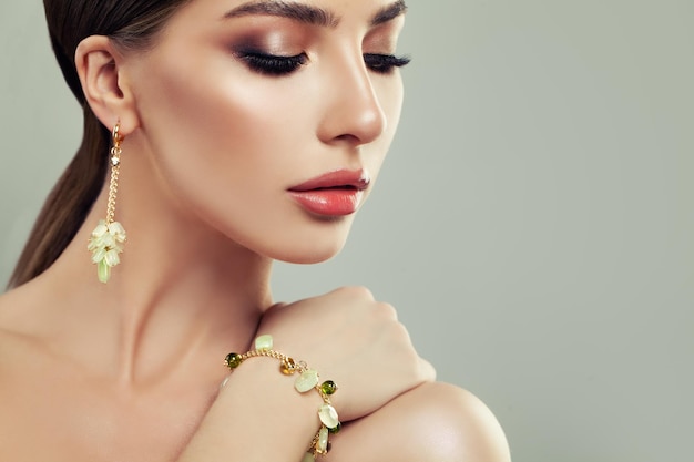 Closeup Portrait of Young Woman with Jewelry Female Face with Makeup Gold Bracelet and Earrings with Green Gem