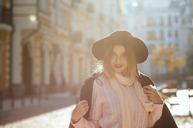 Closeup portret van aantrekkelijke blonde vrouw met hoed en jas poseren met zonlicht. Ruimte voor tekst