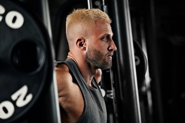 Closeup portret van een gespierde man training met barbell op sportschool. Brutale bodybuilder atletische man met sixpack, perfecte buikspieren, schouders, biceps, triceps en borst.