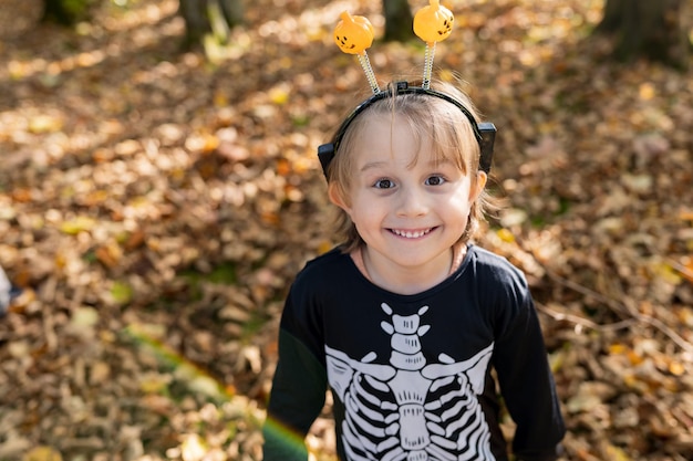 Foto closeup portret van een kleine peuter jongen in halloween skelet carnaval kostuum op droge bladeren in het park in de herfst allerheiligen school herfstvakantie