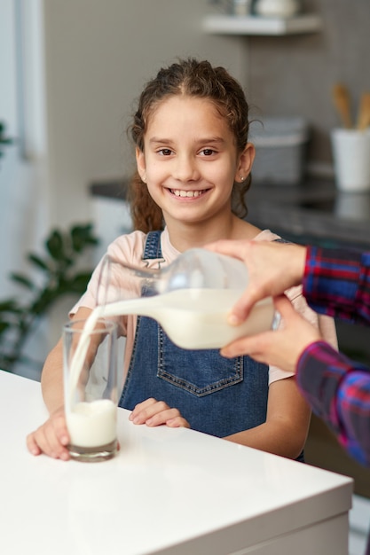 Closeup portret van een moeder giet haar schattige lachende dochter melk voor het ontbijt