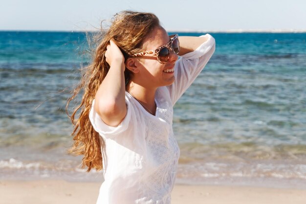 Closeup portret van een mooie jonge brunette meisje met lang haar op een achtergrond van blauwe zee met golven en lucht met wolken op een zonnige dag levensstijl poseren en lachende wind
