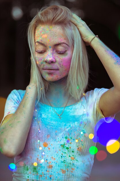 Closeup portret van glorieuze blonde vrouw met droog Holi-poeder op haar gezicht poseren met kleurrijke garland