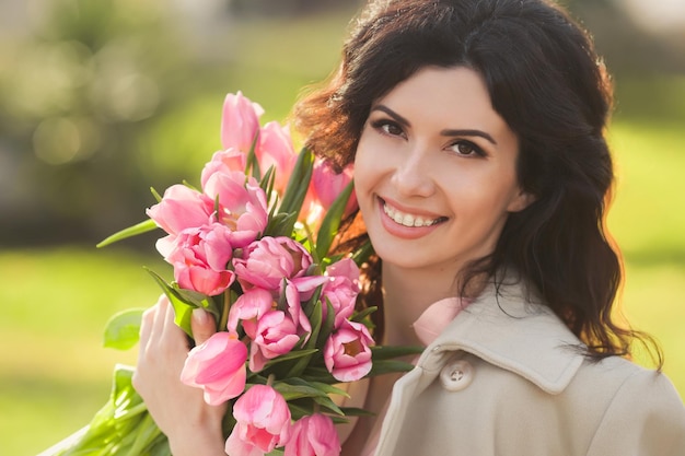 Closeup portret van mooie brunette vrouw die lacht met een beugel met boeket roze tulpen