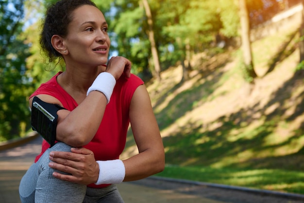 Closeup portret van mooie Spaanse vrouw atleet in sportkleding ontspannen tijdens joggen in het stadspark glimlacht opzij kijkend genietend van ochtendtraining op zonnige zomerdag