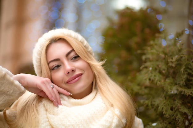 Closeup portret van schattige blonde vrouw met witte gebreide muts en sjaal, poseren op de achtergrond van bokeh