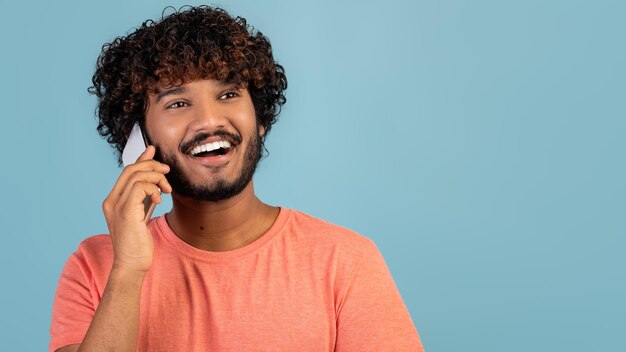 Closeup of positive indian guy having phone conversation on blue