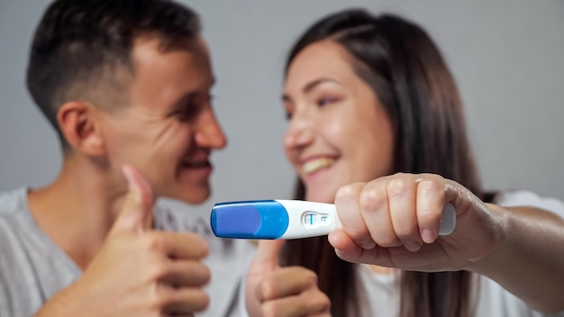 Closeup of positive pregnancy test on blurred background of happy man and woman